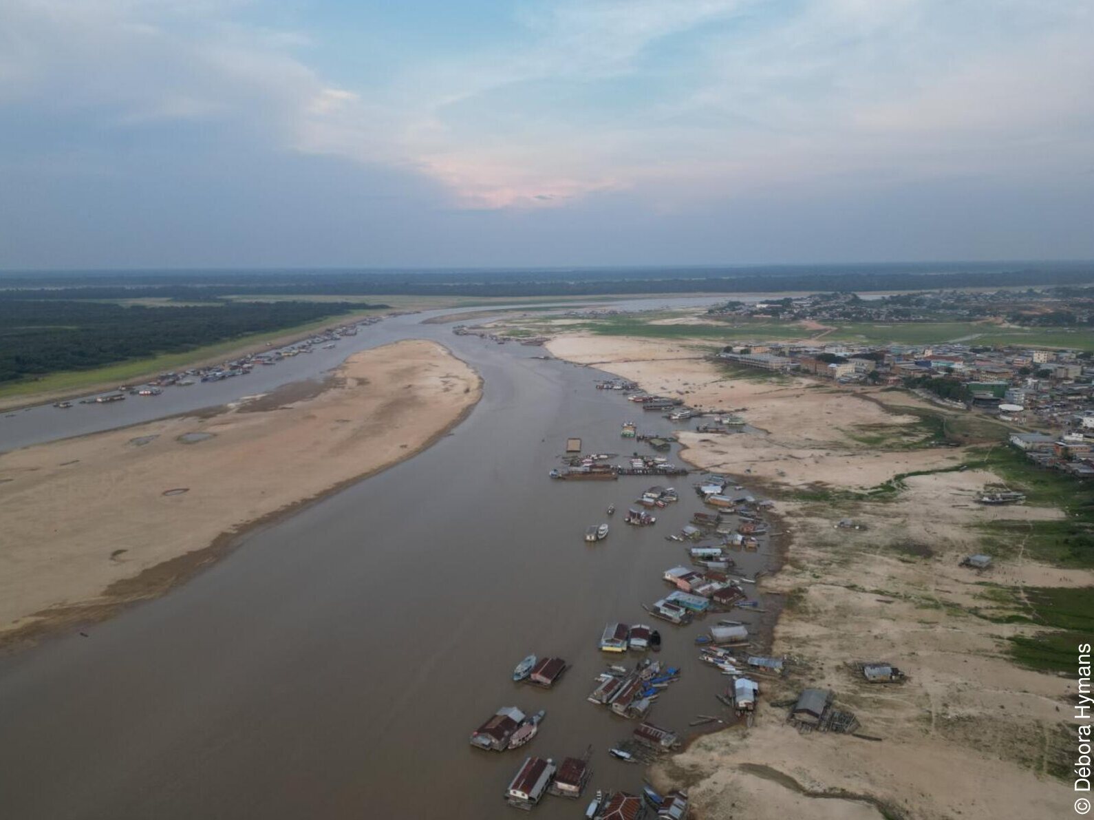 Vista aérea de rio com nível muito baixo, barcos encalhados e uma cidade ao fundo