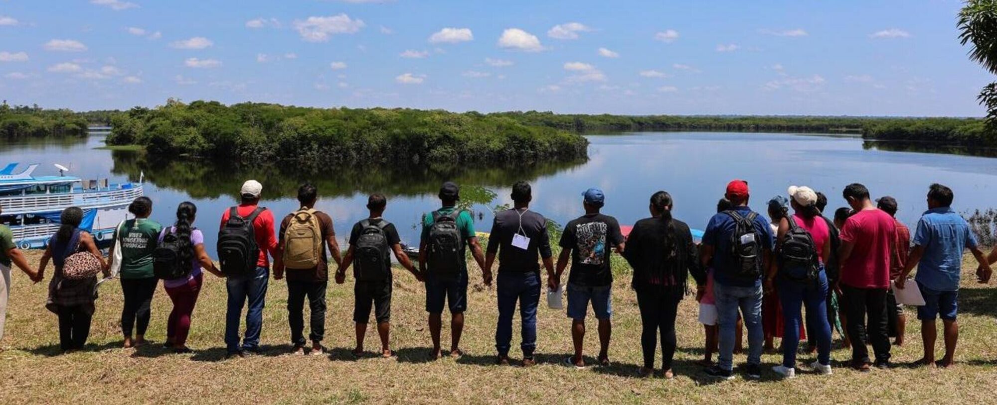 Fileira de comunitários de mãos dadas, de costas, olhando o lago