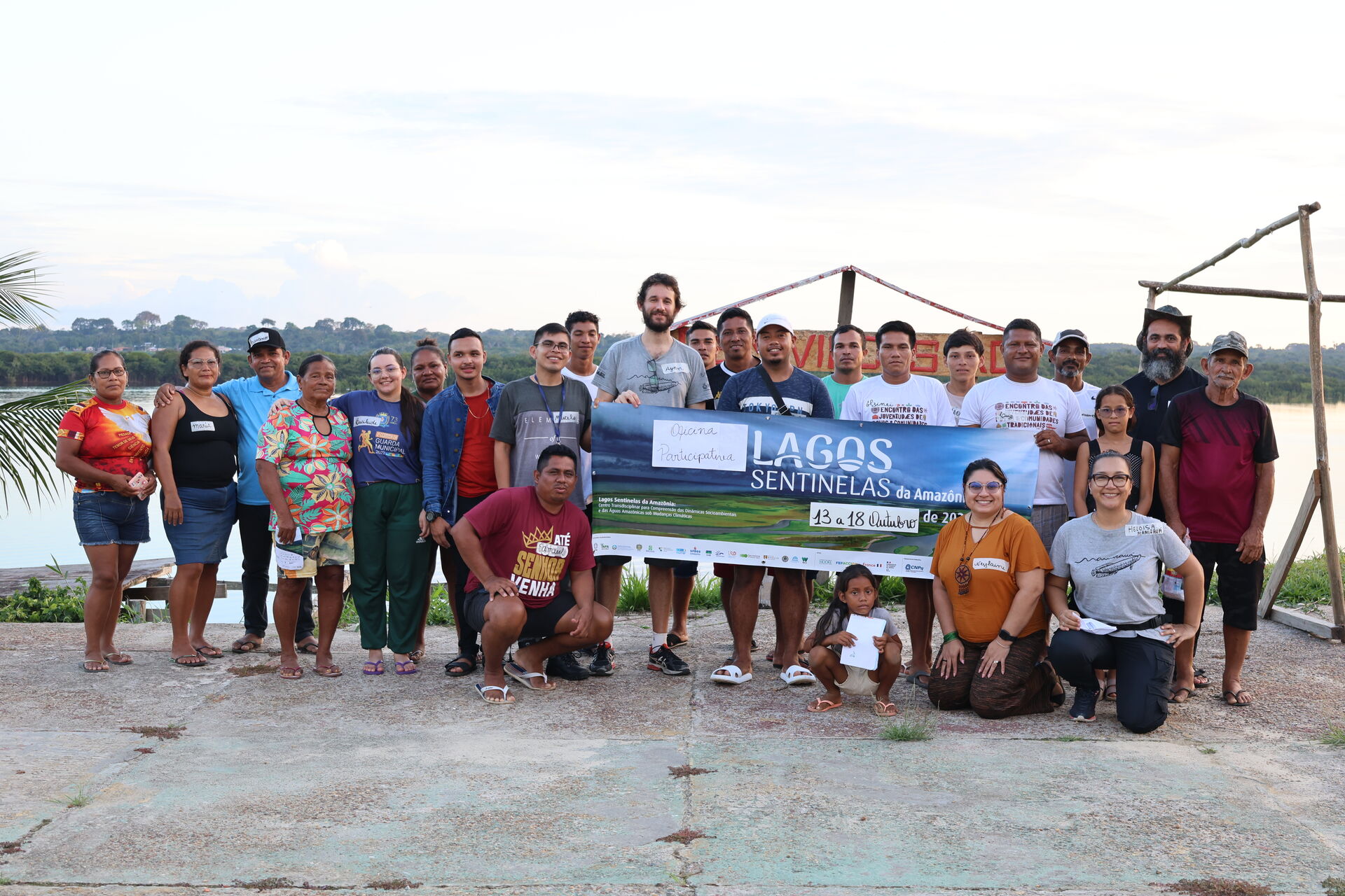 Grupo grande de comunitários e pesquisadores ao ar livre segurando a faixa do projeto, no quilombo São Francisco do Bauana